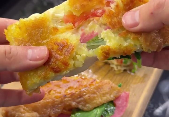 A golden-brown, crispy Turkish potato breakfast wrap (Crunch Bomb) served on a plate, featuring a shredded potato crust, melted cheese, and fresh arugula.