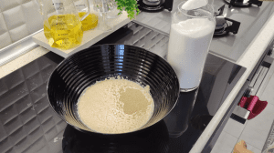 A glass bowl with warm milk, yeast, and sugar becoming bubbly and active.
