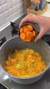 Combining sliced carrots and seared chicken drumsticks in the pot for simmering.