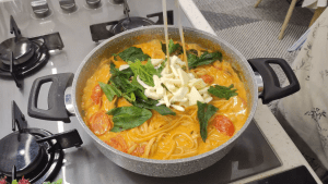 Adding a fresh handful of baby spinach and grated kashar cheese to the cooked creamy pasta.