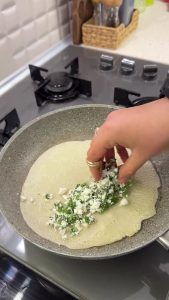 Adding shredded cheese and chopped parsley onto one half of the cooked Turkish flatbread batter.