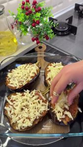 Adding a generous layer of grated kashar cheese on top of the tomato-filled eggplants.