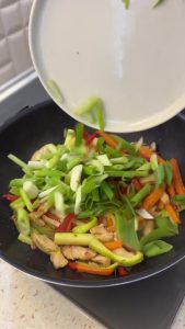 Stirring chopped green onions and garlic into the vegetable and chicken stir-fry.