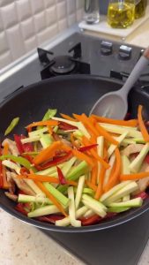 Adding long, thin strips of zucchini and carrots to the chicken and pepper mixture.