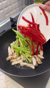 Adding sliced red and green peppers to the skillet with the chicken.