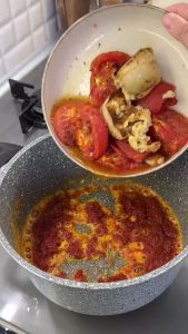 Placing the roasted tomatoes, onions, and garlic into the pot with the tomato paste and flour base.