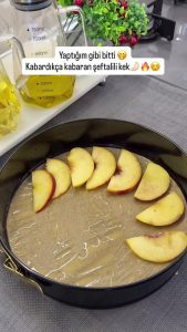 Neatly arranging thin fresh peach slices in a circular pattern at the bottom of the cake pan.