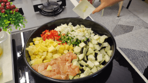 Combining cubed chicken and all vegetables in a large baking tray with crushed tomatoes.