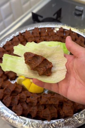 A platter of hand-shaped Turkish meatless çiğ köfte with lettuce and lemon wedges.