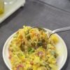 A vibrant yellow curry potato salad with red peppers, corn, and fresh dill in a glass bowl.