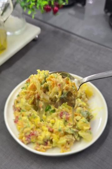 A vibrant yellow curry potato salad with red peppers, corn, and fresh dill in a glass bowl.
