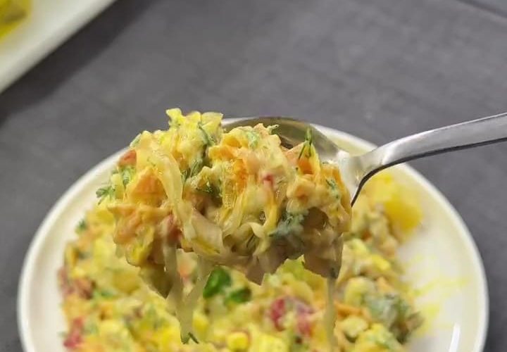 A vibrant yellow curry potato salad with red peppers, corn, and fresh dill in a glass bowl.