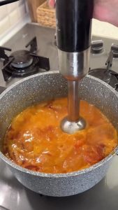 Using a hand immersion blender to process the roasted vegetables into a silky, creamy soup.