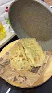 Brushing melted butter onto the golden-brown surface of a crispy Turkish gözleme in a pan.