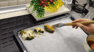 Brushing a red seasoned oil mixture with paprika and pepper onto the flattened broccoli pieces.
