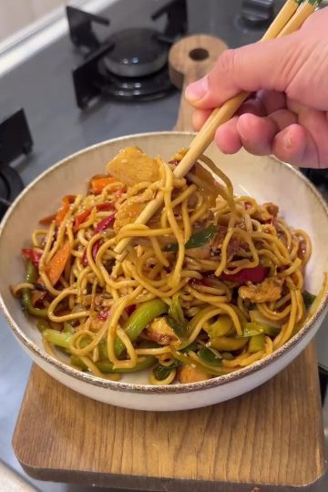 A vibrant plate of chicken and vegetable stir-fry noodles topped with toasted sesame seeds.