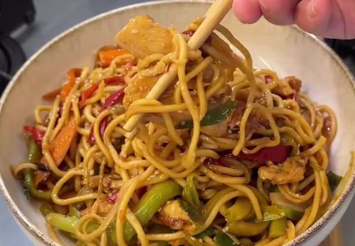 A vibrant plate of chicken and vegetable stir-fry noodles topped with toasted sesame seeds.
