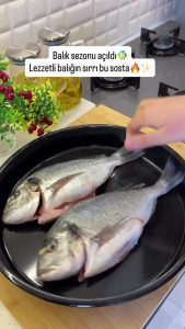 Placing cleaned and washed sea bream fish on a baking tray with parchment paper.