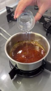 Melting sugar and adding water in a small saucepan to create a smooth, golden caramel sauce.
