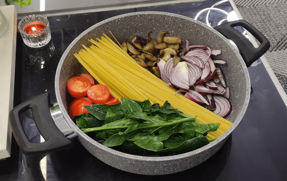 A top-down view of a creamy one-pan linguine pasta with mushrooms, spinach, and melted kashar cheese in a black skillet.