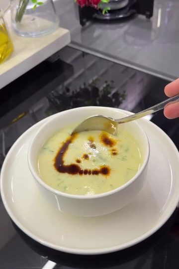 A bowl of creamy Turkish zucchini soup topped with fresh dill and a drizzle of red chili oil.