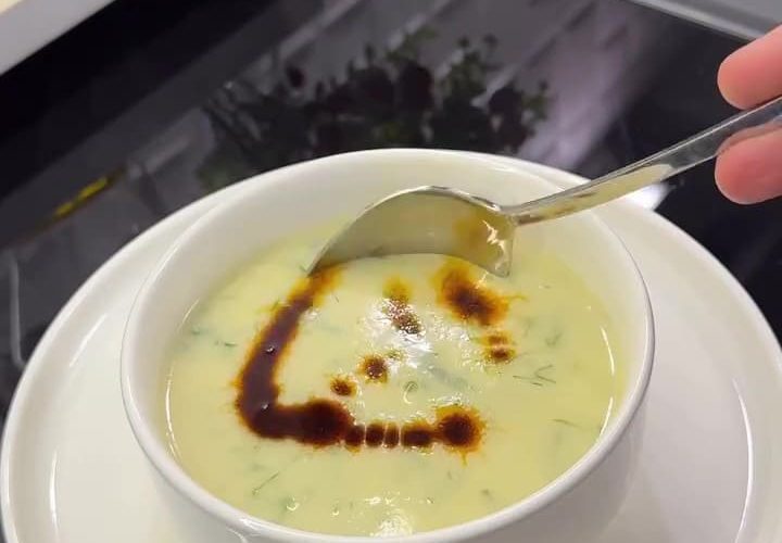 A bowl of creamy Turkish zucchini soup topped with fresh dill and a drizzle of red chili oil.