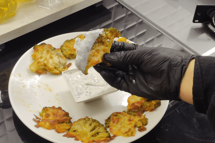 A tray of golden-brown smashed broccoli topped with melted kashar cheese, served with a side of garlic yogurt dip.