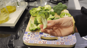 Cutting a head of fresh green broccoli into medium-sized florets on a wooden cutting board.