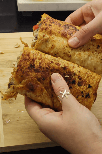 A crispy, golden-brown Turkish fish wrap (Balık Dürüm) sliced in half, showing the grilled mackerel and colorful caramelized peppers inside.