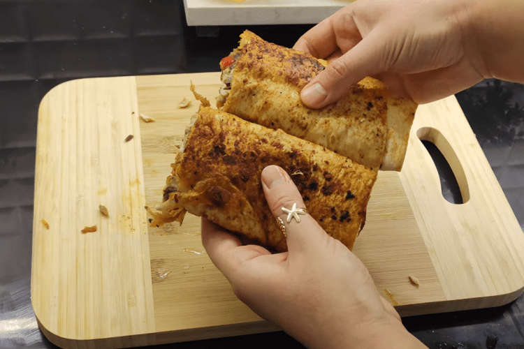 A crispy, golden-brown Turkish fish wrap (Balık Dürüm) sliced in half, showing the grilled mackerel and colorful caramelized peppers inside.
