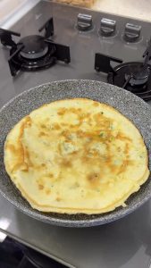 Using a spatula to flip the Kaygana, revealing the perfectly cooked, golden surface underneath.