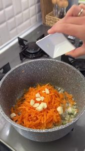 Sautéing grated carrots and onions in butter to create a vibrant golden base for the stew.
