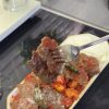 A plate of authentic Turkish İskender Kebap with meat shavings over bread, topped with tomato sauce and melted butter.