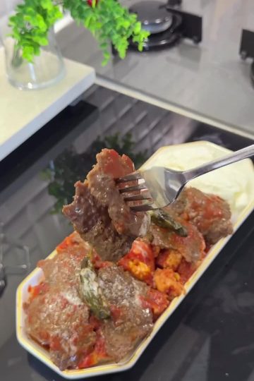 A plate of authentic Turkish İskender Kebap with meat shavings over bread, topped with tomato sauce and melted butter.