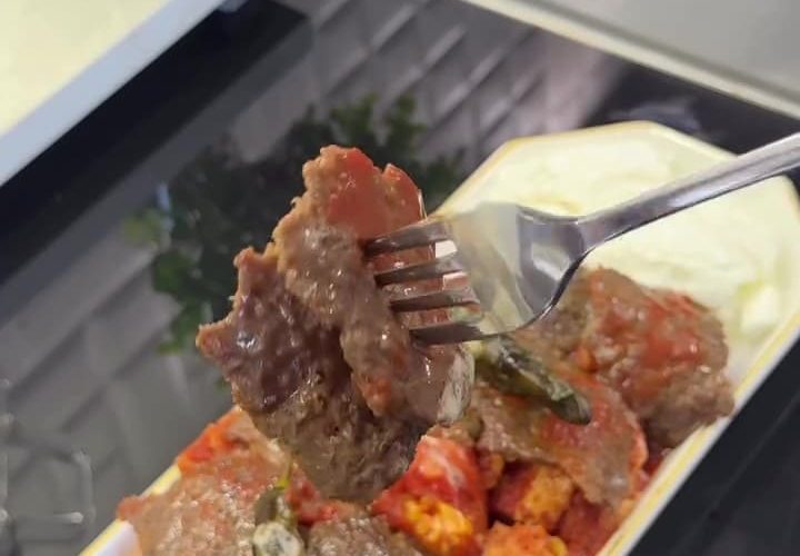 A plate of authentic Turkish İskender Kebap with meat shavings over bread, topped with tomato sauce and melted butter.