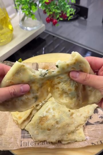 A crispy, golden-brown liquid batter Turkish Gözleme filled with melted cheese and parsley on a serving board.