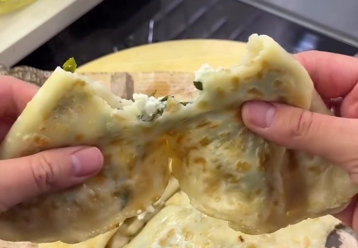 A crispy, golden-brown liquid batter Turkish Gözleme filled with melted cheese and parsley on a serving board.