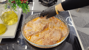 Boneless chicken thighs soaking in a creamy milk, oil, and spice marinade in a bowl.