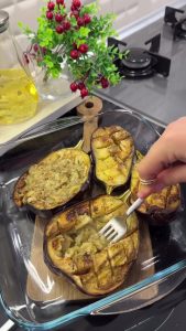 Using a fork to mash the soft centers of roasted eggplants to create a boat shape.