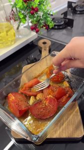 Mashing oven-roasted tomatoes and softened garlic into a rustic sauce using a fork.