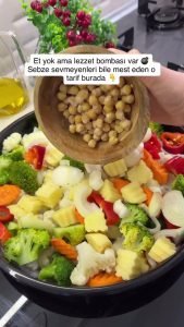 Arranging chopped carrots, potatoes, onions, peppers, and chickpeas on a baking sheet lined with parchment paper.