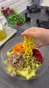 Combining boiled potatoes, sautéed carrot mixture, corn, and chopped roasted peppers in a bowl.