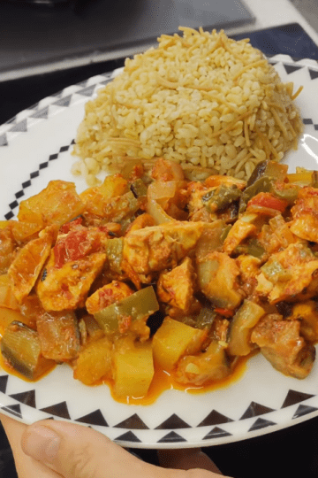 A colorful baking tray filled with roasted chicken cubes, eggplants, potatoes, and peppers in a rich tomato sauce.