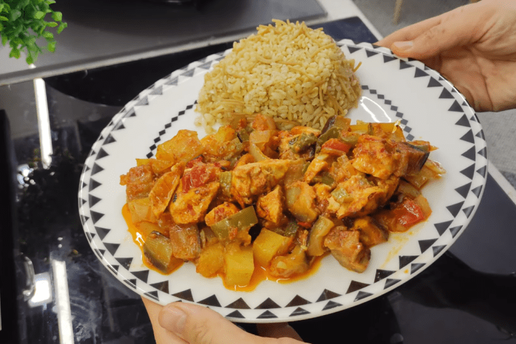 A colorful baking tray filled with roasted chicken cubes, eggplants, potatoes, and peppers in a rich tomato sauce.
