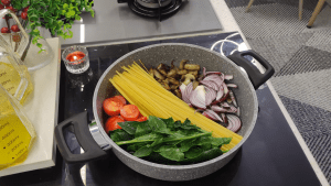 Dry linguine pasta, sliced red onions, and cherry tomatoes arranged in a pan with sautéed mushrooms.
