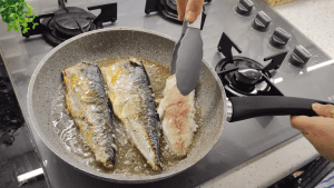 Pan-searing fresh mackerel fillets in a frying pan until they are perfectly golden brown.