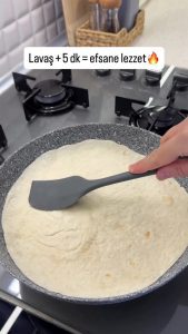 Placing a fresh tortilla (lavaş) directly over the partially cooked eggs in a skillet.