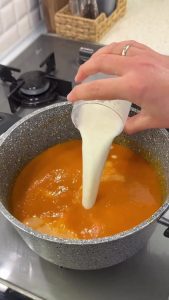Gradually stirring a cup of milk into the blended tomato soup to achieve a velvety consistency.