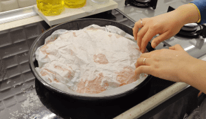 Pouring a red tomato sauce over the arranged cabbage bundles in a tray.