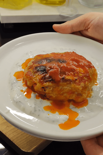 A close-up shot of golden-brown oven-baked cabbage bundles served with garlic yogurt and fresh parsley.